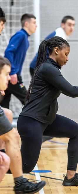 A female student leading a lunge stretch during a group fitness session in a sports hall. A female student leading a lunge stretch during a group fitness session in a sports hall.